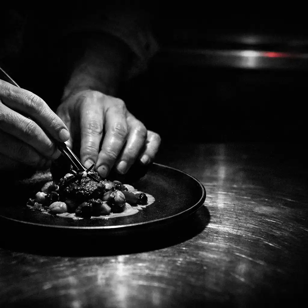 Hands finishing a plate at a dark restaurant pass.