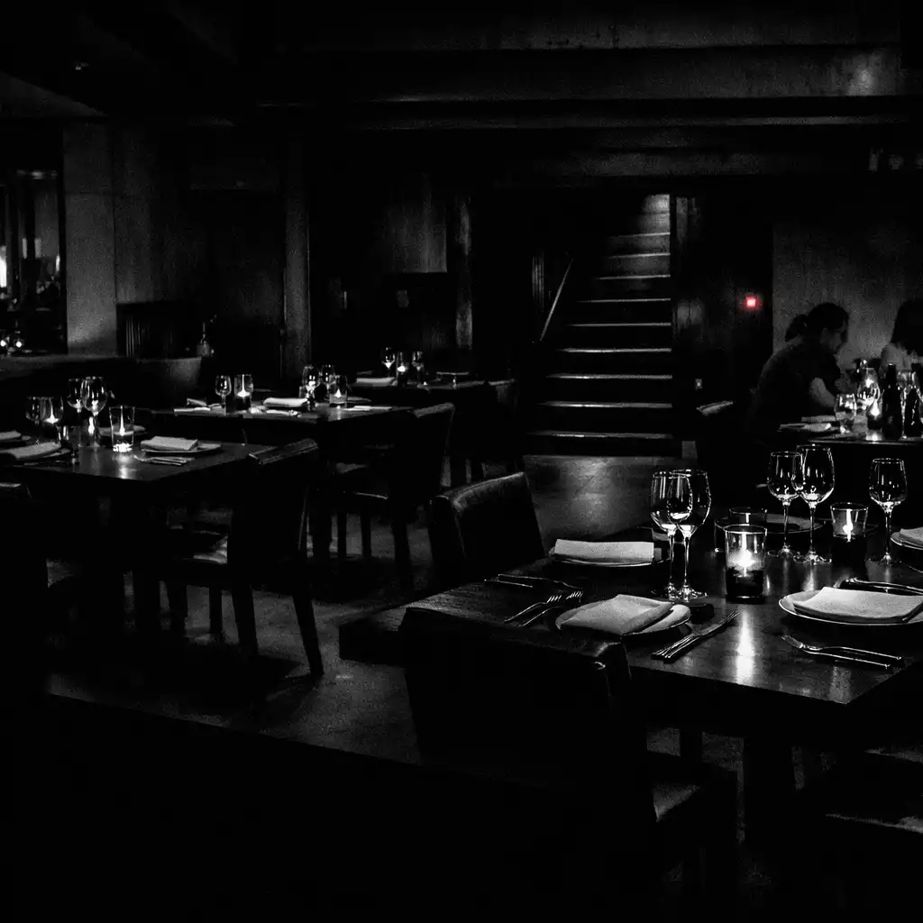 A dark TABLE QIRON dining room viewed across closely arranged tables.