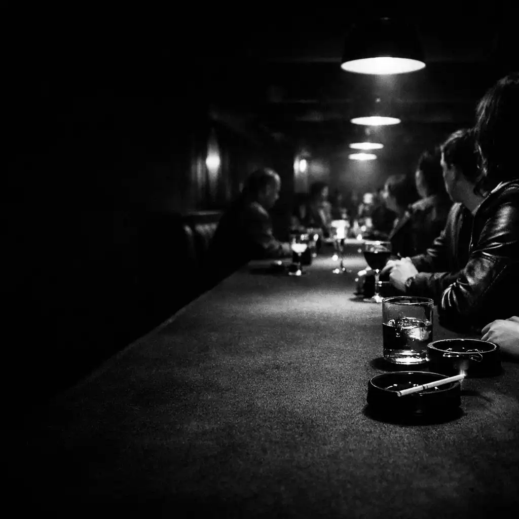 A long table receding through a dark underground restaurant lounge with glasses and cropped guests.